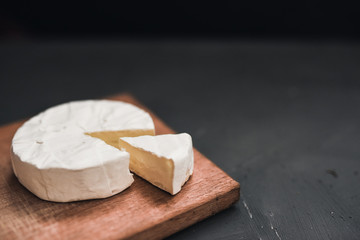 Camembert round cheese and a slice lie on a wooden board. grey matte concrete background.