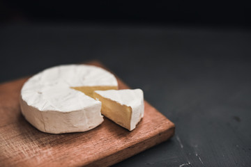 Camembert round cheese and a slice lie on a wooden board. grey matte concrete background.