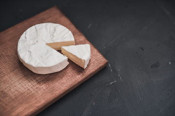 Camembert round cheese and a slice lie on a wooden board. grey matte concrete background.