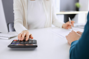 Accountant checking financial statement or counting by calculator income for tax form, hands closeup. Business woman sitting and working with colleague at the desk in office toned in blue. Tax and