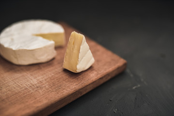 Camembert round cheese and a slice lie on a wooden board. grey matte concrete background.