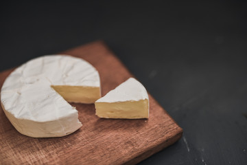 Camembert round cheese and a slice lie on a wooden board. grey matte concrete background. 