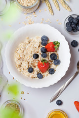 Oatmeal porridge with strawberry, blueberry, flax seeds and honey on gray background.