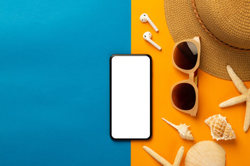 Summer background with blank screen smartphone and beach accessories - sunglasses, straw hat on vibrant orange and blue background top view with copy space.