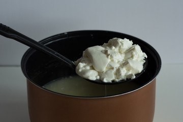 Skimmer with mess of fermented cheese or cottage cheese or greek yogurt taking it from pan to put...