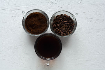 Three cups of ground coffee, coffee beans and brewed coffee in one row