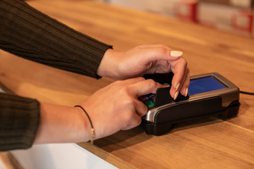 A pin machine on a counter. A woman blocking her pin code with her hands so scammers can’t use her bank card. Privacy protection while purchasing