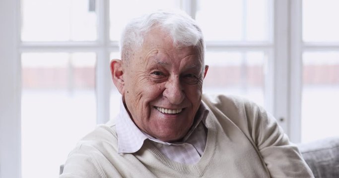 Close up head shot happy middle aged older man with healthy white teeth looking at camera. Portrait of smiling excited elderly mature single grandfather relaxing indoors at home or retirement house.