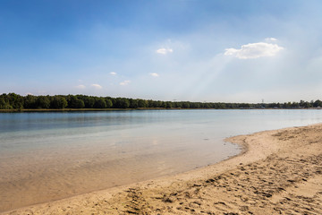 A lake and beach in the Netherlands used for recreation, swimming and sunbathing in Brabant. Calm water, greenery, sand and a blue sky. Relaxation