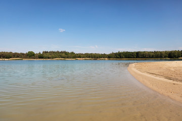 A lake with a beach in the Netherlands used for recreation, swimming and sunbathing in Brabant. Calm water, greenery, sand and a blue sky. Relaxation