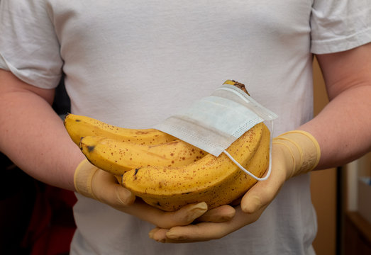 Bananas and a medical face mask in the hands of a man in rubber gloves. Fruits, harvest 2020, pandemic, coronavirus. Contactless food delivery.
