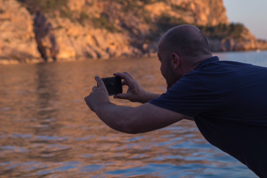 A man taking photos at sunset in Cala Llamp with his Mallorca mobile phone. Beach cove in Mallorca