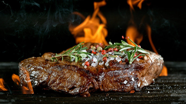 Tasty beef steak on cast iron grate with fire flames. Freeze motion barbecue concept.
