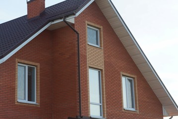 the attic of a red brick house with white windows under a brown tiled roof against a gray sky