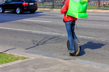 A courier with an isothermal green backpack behind him on an electric monowheel with food delivery. © Sergii