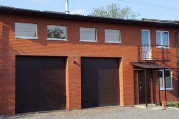 two brown gates on a red brick wall of a garage with windows on the street