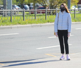 A girl in a medical mask, dark glasses and disposable gloves on the street, ulitsa Kollontai, Saint Petersburg, Russia may 2020