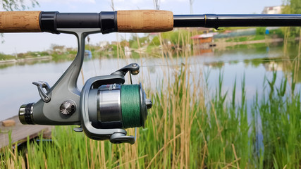 Fishing reel on a spinning comel close-up on the background of a lake or river. Reel with green fishing line on a natural background. Fisherman's equipment. Copy space. Natural background.