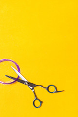 Hairdressing scissors with a strand of purple hair on a yellow background