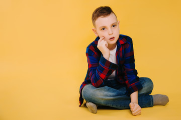 A boy in a plaid shirt sits on a yellow background. Studio photo of a child
