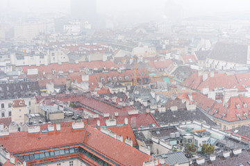 Fototapeta premium Cityscape with red tiles rooftops of the old town of Vienna in a heavy snowy day. View at the tower of St. Stephen's Cathedral in Vienna, Austria.