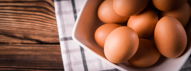 Banner detail close-up of chicken eggs on the old brown wooden background.