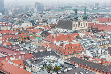 Obraz premium Cityscape with red tiles rooftops and tower of Jesuit Church of the old town of Vienna in a heavy snowy day. View at the tower of St. Stephen's Cathedral in Vienna, Austria.