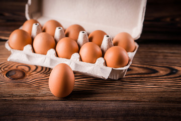 Detail close-up of chicken eggs in egg box on the old brown wooden background.