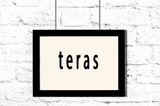 Black frame hanging on white brick wall with inscription teras