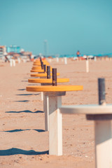 Fototapeta na wymiar A row of yellow beach tables set at safety distance. Preparing the beach for the season after COVID emergency lockfown. Setting tables at safety distance. Vintage feel.