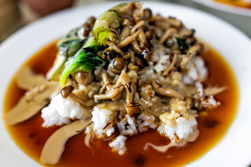 Traditional plate vegetable japanese dish in Japan with mushrooms and spinach greens on pile of white rice and soy sauce on white plate closeup