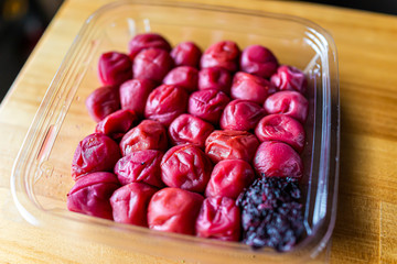 Traditional japanese storebought packaged red umeboshi pickles made with ume plum closeup on wooden table with pink shiso leaf