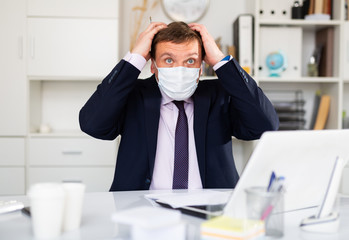 Dissatisfied man in protective mask working at office