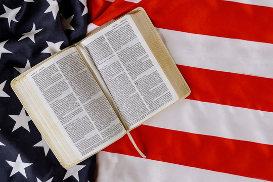 American flag ruffle with open is reading Holy Bible book with prayer for america over US flag - Powered by Adobe