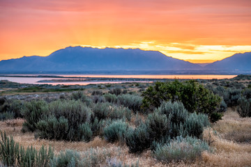 Orange red yellow sunlight sunrise on Great Salt Lake in Antelope Island State Park Ladyfinger campground with reflection on water and sun rays