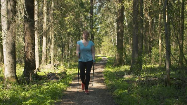 Mature woman with trekking poles walking in the forest. Exercising in nordic walking, active and healthy lifestyle concept
