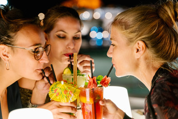 Women drinking cocktails together on a terrace at night