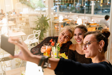 Profile of women making a selfie while sitting on a terrace drinking cocktails at night