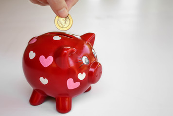 hucha de cerdito de color rojo y corazones rosas con una mano poniendo un euro para ahorrar