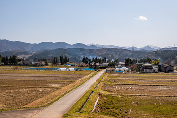 Toyama, Japan countryside road near Gifu prefecture with traditional farm houses and brown field for crops and mountains in view photographed from train in spring