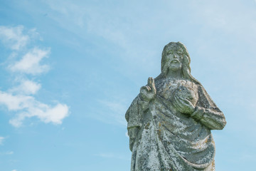 Very old stone statue of Jesus Christ against blue sky. Faith, religion, death, resurrection concept.