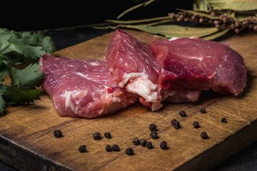 Cooking concept. three pieces of meat (pork) are laid on top of each other on a wooden board. Around the meat are spices, bay leaves, cilantro and a slice of tomato. photo near