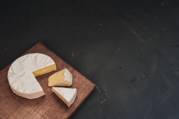 Camembert round cheese and a slice lie on a wooden board. grey matte concrete background. 