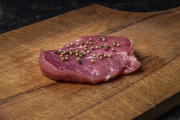 Cooking concept. one piece of meat (pork) lies on a wooden board. On top of the meat is sprinkled with coriander. photo on a black background.
