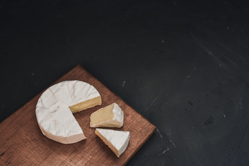 Camembert round cheese and a slice lie on a wooden board. grey matte concrete background. 
