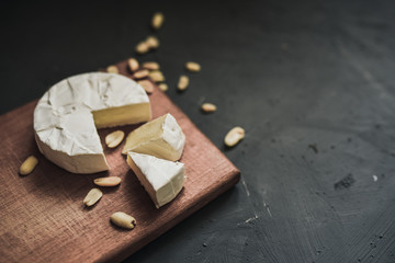 Camembert round cheese and a slice lie on a wooden board. grey matte concrete background. peanut