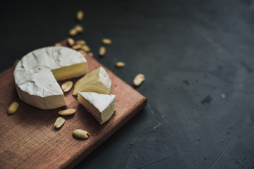 Camembert round cheese and a slice lie on a wooden board. grey matte concrete background. peanut