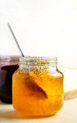 homemade orange marmalade spoon picking jam from a glass jar, sweet breakfast over light wooden background with copy space