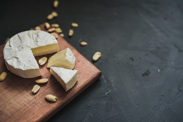 Camembert round cheese and a slice lie on a wooden board. grey matte concrete background. peanut