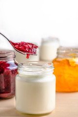 Homemade yogurt with red berries marmalade spoon picking from a glass jar on a white wooden table. Healthy dairy probiotic breakfast with copy space